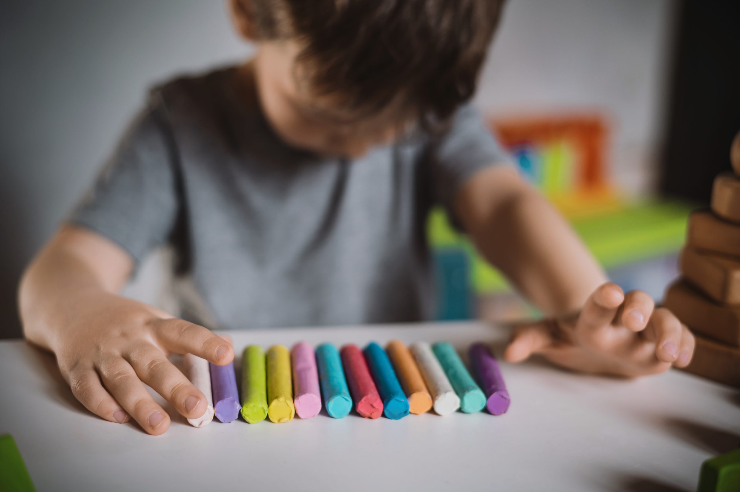 A little boy of three years sits at a table with colored crayons a young girl holding a leaf