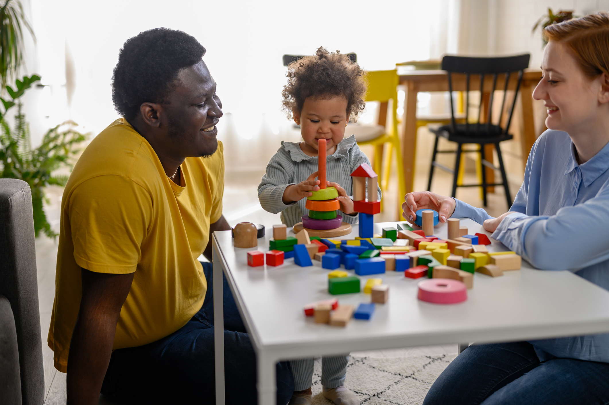 Mother and father supporting their cute little daughter in playing with colorful didactic wooden toys at home